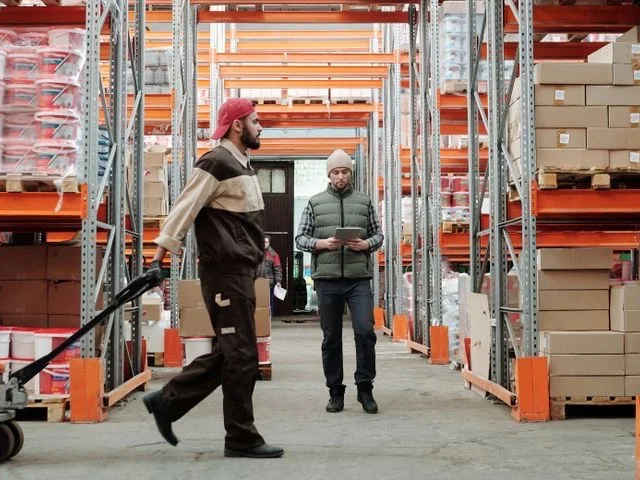Bolti előkészítők árut mozgatnak a raktár folyosóján kézikocsival
